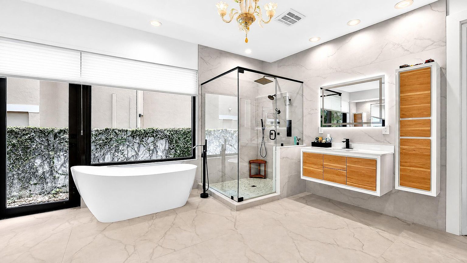 Wide view of the primary bath: soaking tub, glass shower, floating vanity and chandelier