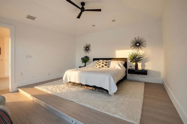 Primary bed on a raised platform with an area rug and a ceiling fan