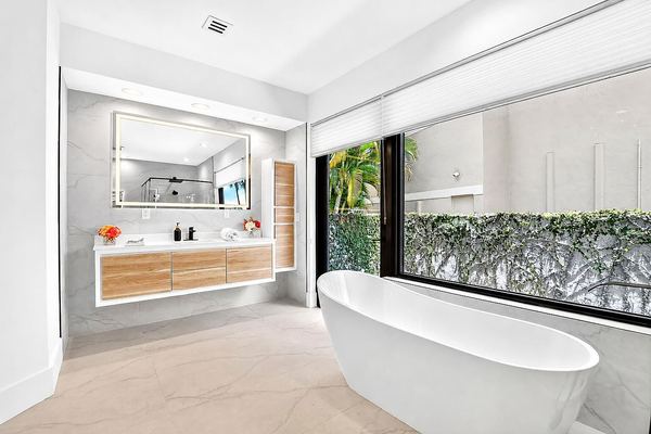 Freestanding soaking tub beside a picture window framed by greenery