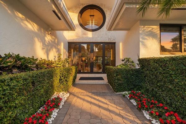 Front entry walkway with a round window, clipped hedges and red flowers